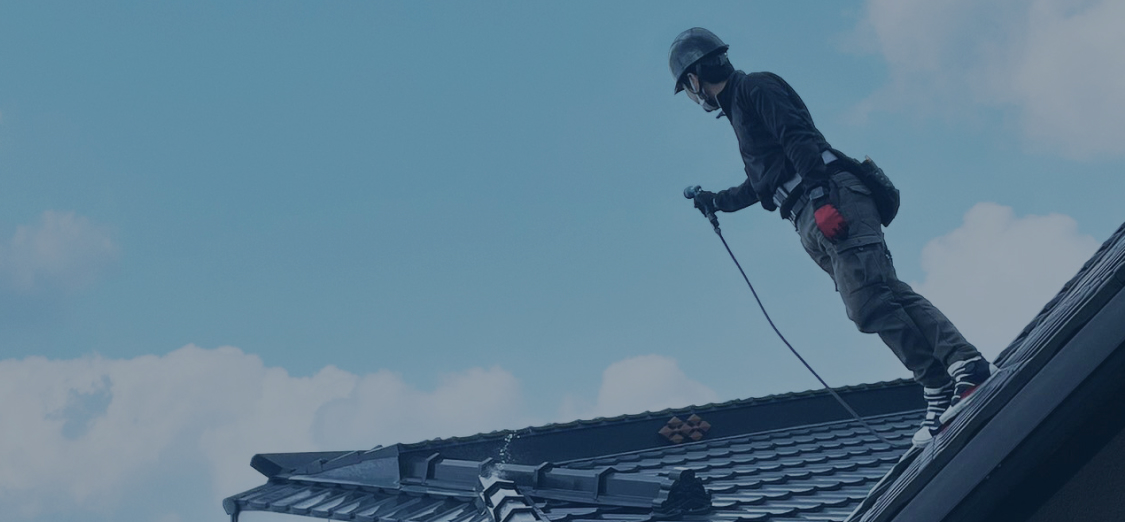 空をバックに屋根の上にヘルメットを被った作業員が立っている