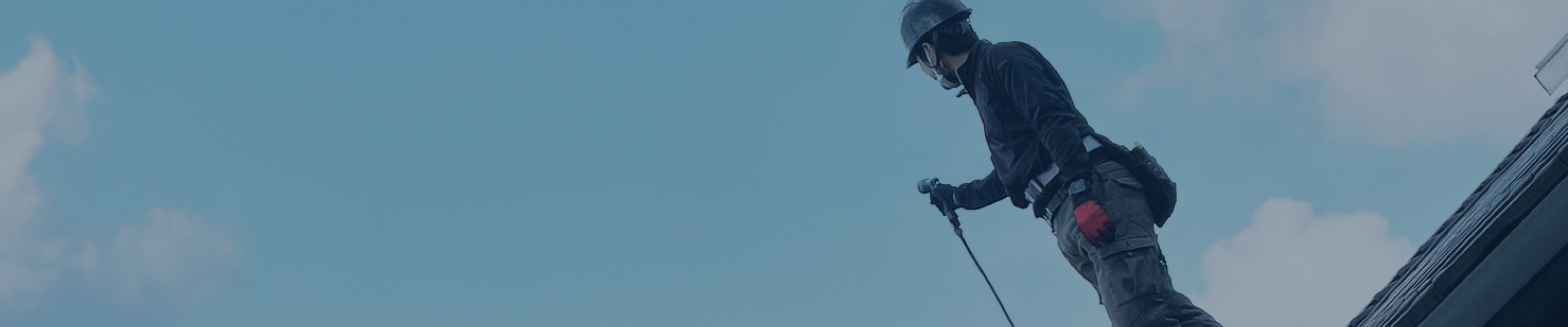 空をバックに屋根の上にヘルメットを被った作業員が立っている